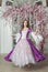 Beautiful woman in fantasy white and purple rococo style medieval dress dancing near door with pink flowers