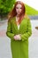 Beautiful woman with fiery red hair with green coat walking through the streets of the city