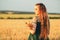 Beautiful woman in green dress on field with sheaf of wheat in hand at sunset light, girl enjoying summer nature landscape,