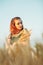 Beautiful woman in green dress on field with sheaf of wheat in hand at sunset light, girl enjoying summer nature landscape,