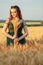 Beautiful woman in green dress on field with sheaf of wheat in hand at sunset light, girl enjoying summer nature landscape,
