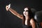 Beautiful woman with Halloween makeup and balloons taking selfie near dark brick wall