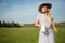 Beautiful woman in a hat and dress holds bread and a carafe of milk in her hands. Standing on the lawn against the sky natural