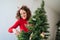 A beautiful woman having fun while decorating a Christmas tree at home. She is putting a Christmas ornament on the tree. She is