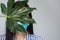 Beautiful woman hides face in a medical mask and open her eyes with big green tropical leaf, Faceless, Protection from covid