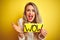 Beautiful woman holding amazed wow surprise banner over isolated yellow background very happy and excited, winner expression