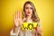 Beautiful woman holding amazed wow surprise banner over  yellow background with open hand doing stop sign with serious and