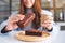 A beautiful woman holding and eating a piece of brownie cake while drinking coffee