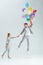 beautiful woman holding hand of man jumping in air with bundle of colorful balloons