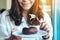 A beautiful woman holding and using fork to eat chocolate donut in a white plate