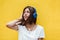 Beautiful woman joyful listening to music on headsets. Yellow background