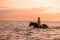 Beautiful woman joyfully riding a horse through a body of water at sunset