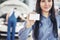 A beautiful woman keeps a business card of the car service center. The mechanic inspects the car under the hood in the