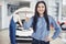 A beautiful woman keeps a business card of the car service center. The mechanic inspects the car under the hood in the