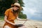 Beautiful woman with a laptop sits on the sand and works