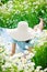 A beautiful woman in a large straw hat covering her face lies on a field of daisies. Enjoys nature and spring time