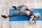 Beautiful woman is laying on blue mat, doing yoga at home, working out for wellness. Athletic lady in sportive wear