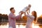 Beautiful woman lifts high her adorable baby girl up mid air and looks at her smiling. Happy parents spending time playing with
