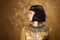 Beautiful woman like Egyptian Queen Cleopatra on golden background. Side view, face profile
