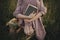 Beautiful woman in linen dress sitting barefoot on rustic chair with book in summer meadow, close up