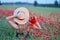 Beautiful woman with long blond hair in hat walking in the field with poppies