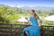 Beautiful woman with long blond hair in a long blue dress with a glass of sparkling wine sitting on the railing of the balcony aga