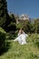 a beautiful woman with long brown hair and long white dress stay along a path along beautiful bushes in the park rear