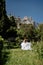 a beautiful woman with long brown hair and long white dress stay along a path along beautiful bushes in the park rear