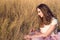 Beautiful woman with long hair wearing white silk top and pink veiling skirt sitting in the yellow field and touching dried grass