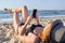 Beautiful woman lying on the beach and looking at the smartphone on sea bsckground