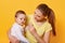 A beautiful woman on maternity leave and her cute little daughter hug each other on bright yellow background. A sweet child looks