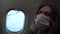 A beautiful woman in a medical mask is flying on a plane.