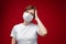 Beautiful woman with medical mask is sick coughs and sneezes, picture isolated on red background