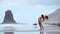 A beautiful woman on the ocean beach with black volcanic sand performs gymnastic exercises practicing a healthy