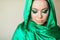 A beautiful woman of Oriental appearance with make up on her face in a shiny green scarf covering her head closed her eyes.