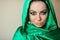 A beautiful woman of Oriental appearance with makeup on her face in a green shiny scarf covering her head.