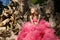 Beautiful woman in pink evening dress with fluffy aerial skirt is posing in botanical garden on the driftwood