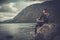 Beautiful woman posing on the shore of a wild lake, with mountains on the background.