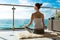 The beautiful woman practicing yoga on a rug and sitting on a balcony with the seaside view.