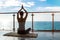 The beautiful woman practicing yoga on a rug and sitting on a balcony with the seaside view.