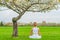 Beautiful woman is practicing yoga sitting in Lotus pose near blossom tree