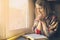 Beautiful woman praying having the Bible opened in front of the window