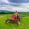 Beautiful woman on a red agricultural tractor, green field, landscape of meadow with grass Upstate New York