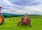 Beautiful woman on a red agricultural tractor, green field, landscape of meadow with grass Upstate New York