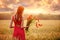 Beautiful woman in a red dress with a bouquet of poppies in a wheat field at sunset, warm toning, happiness and a healthy lifestyl