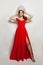 Beautiful woman in red dress puts on diamond crown against white wall background