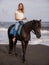 Beautiful woman riding horse on the beach. Outdoor activities. Caucasian woman wearing jeans and white T-shirt. Traveling concept