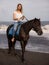 Beautiful woman riding horse on the beach. Outdoor activities. Caucasian woman wearing jeans and white T-shirt. Traveling concept