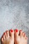 Beautiful woman& x27;s red nails with beautiful pedicure. Female feet with bright pedicure on grey concrete background