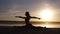 Beautiful woman`s silhouette doing yoga, split on sea coast. Morning sunrise, smog sun on thee backstage